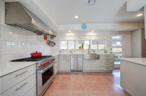 White kitchen cabinets, pink terrazzo floor, stainless farm sink and Wolf stove